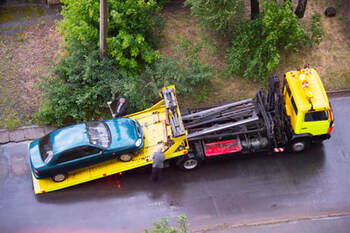 Yellow flat bed tow truck towing away a green car. 